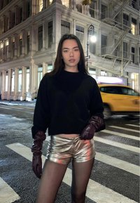 Black cropped sweater, metallic silver shorts, and burgundy leather gloves. Urban nighttime setting with street signs and yellow taxi.