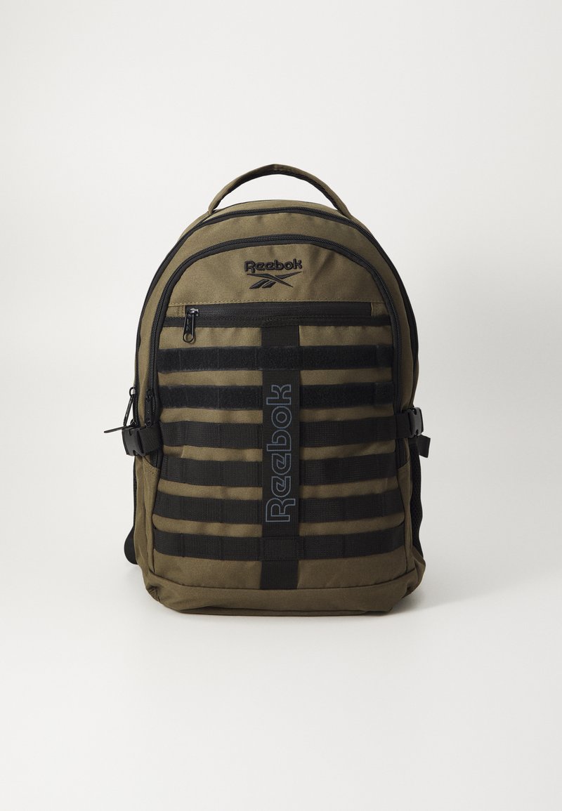 Mochila verde oliva com detalhes em preto estriado, apresentando um bolso frontal com zíper e o logo da Reebok na parte superior. Material resistente e alças ajustáveis.