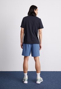 T-shirt en coton noir, short bleu, baskets de sport avec accents verts. Design simple, coupe décontractée, coutures visibles et manches courtes.