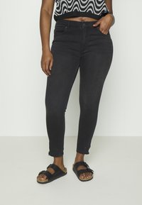 Jeans skinny pretos com um ligeiro stretch, bainha desfiada e bolsos, combinados com sandálias pretas com fivela e sola de cortiça.