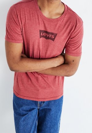T-shirt rouge chiné à manches courtes avec un col rond et un logo Levi's noir imprimé sur le devant. Le tissu semble doux et légèrement texturé.