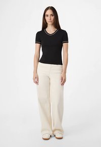 Svart kortärmad topp med V-ringning och vit kant, kombinerad med vida cremefärgade byxor, vilket skapar en kontrasterande minimalistisk look.