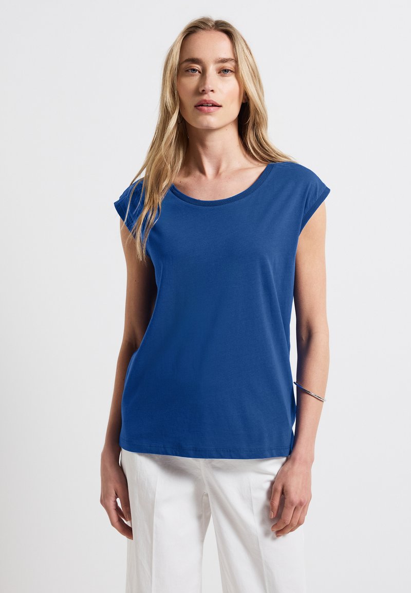 Blå kortärmad t-shirt med rund halsringning och en avslappnad passform, tillverkad av mjukt tyg. Kombinerad med vita byxor, minimalistisk design.