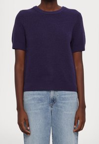 Fialový krátký pletený svetr s žebrovanou texturou, kulatým výstřihem a přiléhavým lemem, kombinovaný se světlými modrými džíny z denimu.