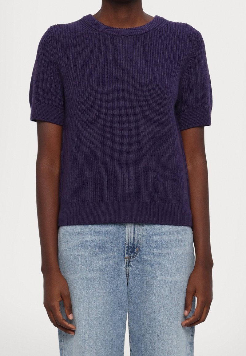 Fialový krátký pletený svetr s žebrovanou texturou, kulatým výstřihem a přiléhavým lemem, kombinovaný se světlými modrými džíny z denimu.