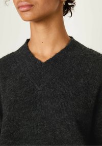 Dark gray knitted sweater with a V-neck design, featuring a soft, textured finish and slightly loose fit. Minimalist style with no embellishments.