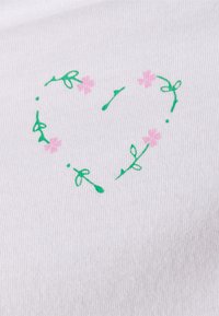 O tecido branco apresenta uma forma de coração desenhada à mão, composta por vinhas verdes e pequenas flores cor-de-rosa, com uma superfície texturizada e estriada.