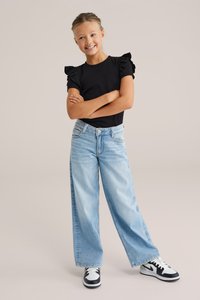 Černé žebrované tričko s volánovými rukávy, v kombinaci se světle modrými širokými jeany. Černobílé tenisky dokončují celý outfit.