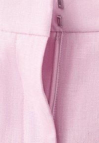 Tela rosa en primer plano que muestra una cremallera oculta y dos cierres de gancho y ojo plateados sobre un material tejido y texturizado.