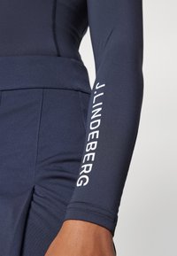 Tengerészkék, hosszú ujjú felső, amely fitted szabású, sima anyagból készült, fehér "J.LINDEBERG" logóval a jobb karon.