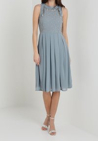 Ljusblå klänning med veckad kjol och utsmyckad bodice. Har volangdetaljer på axlarna. Bärs med silverfärgade klackar med ankelrem.