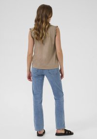 Haut beige sans manches avec des accents en volants, associé à un jean droit bleu clair et des sandales à lanières noires. Tenue simple et décontractée.