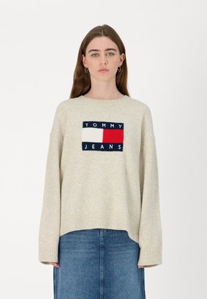 Maglione beige lavorato a maglia con scollatura ampia, caratterizzato da un logo rettangolare navy, bianco e rosso sul davanti. Polsini e orlo a coste.