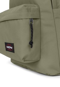 Zelený látkový batoh s přední kapsou, černým zipem a texturovaným povrchem. Obsahuje černou nášivku loga Eastpak.