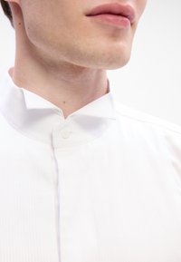 Balta apkakles krekla ar elegantu dizainu, kas ir ar vertikālām svītrām un vienu pogu aizdari apkaklē. Gluda tekstūra.