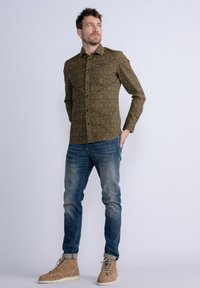 Bruine gebloemde langemouwen shirt, denim jeans en beige suède laarzen. Het shirt heeft een bloemenpatroon; de jeans zijn nauwsluitend met een vervaagde afwerking.