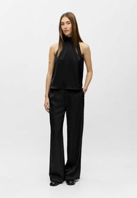 Schwarzes Satin-Haltertop kombiniert mit locker sitzenden schwarzen Hosen, die eine fließende Silhouette und eine glatte Textur schaffen. Einfaches, minimalistisches Design.