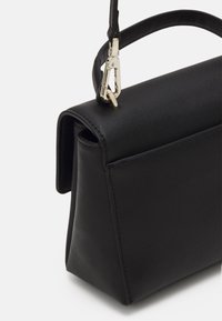 Černá kožená kabelka s pevnou strukturou, zaoblenými hranami a krátkým držadlem. Má zlaté kovové doplňky a minimalistický design.