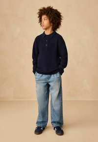 Marineblauer Strickpullover mit Kragen und drei Knöpfen, kombiniert mit locker sitzenden hellblauen Denim-Jeans und navy Sneakern.
