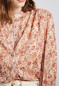 Chemise à boutons florale en tissu léger et doux; présente un fond pêche avec des motifs rouges et jaunes complexes et un col classique.