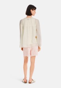 Helles gelbes Bluse mit gerafftem Rücken, kombiniert mit rosa strukturierten Shorts. Die Bluse hat lange Ärmel und einen lässigen Schnitt.