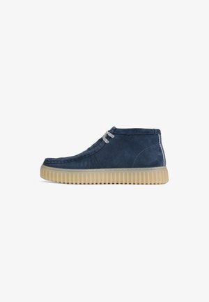 Stivali alla caviglia in suede blu navy con superficie texture, lacci grigi e suola in gomma beige con scanalature per maggiore aderenza.