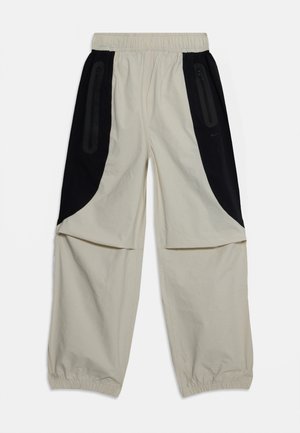 Pantalons beiges avec des panneaux latéraux noirs, taille élastique et poches zippées, présentant une coupe décontractée et un tissu doux et léger.
