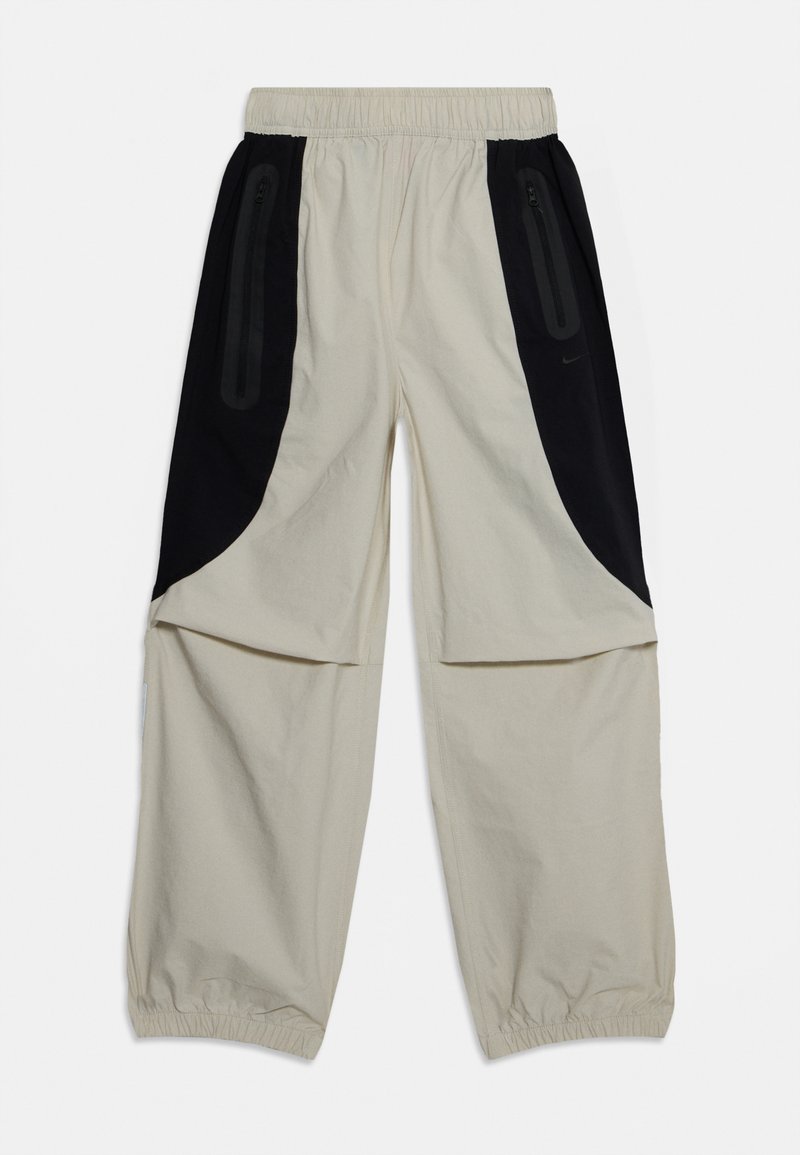 Beige Hose mit schwarzen Seitenpanelen, elastischem Bund und Reißverschlusstaschen, ausgestattet mit einem entspannten Schnitt und weichem, leichtem Stoff.