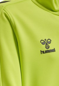 Limoengroene langetoe top van getextureerde stof, met een zwart "hummel" logo op de borst en een hoge kraag.