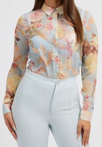 Chemise transparente boutonnée en bleu clair avec des motifs floraux en rose, orange et vert ; colée, manches longues et poignets à un seul bouton.