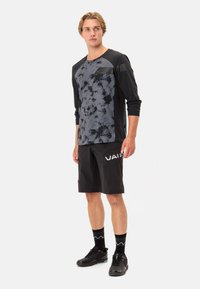 Langermet svart og grå tie-dye topp, lett stoff; svarte shorts med sidelommer, "VALID" logo i hvitt, kombinert med svarte joggesko.