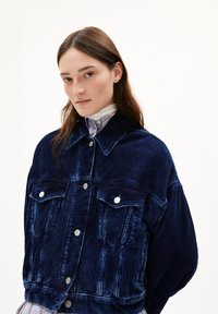 Giacca di velluto a coste blu navy con due tasche frontali, bottoni argentati e un fit rilassato. La texture è caratteristicamente a costine e morbida.
