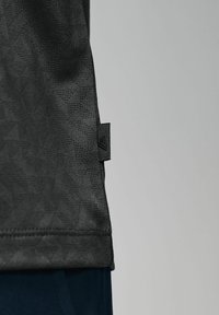 Sort kortærmet skjorte med et tekstureret, geometrisk mønster, der har et lille logo-tag i kanten. Materialet ser let og åndbart ud.