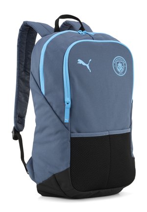 Mochila Puma azul y negra con cremalleras azul claro y logo de Manchester City en el bolsillo delantero.
