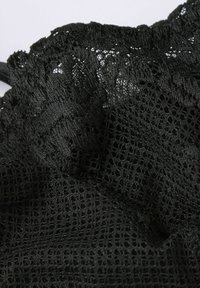 Tissu en maille noire avec un motif texturé et à tissage ouvert, présentant des fils lâches et des bords élastiques. Convient aux applications de vêtements légers.