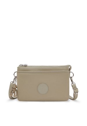Bolso bandolera beige con cierre de cremallera, material de tela, diseño plano, parche de logo redondo y un adorno decorativo unido a la correa.