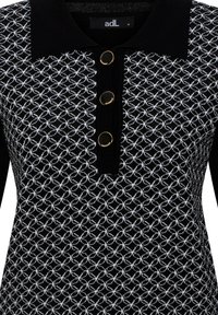 Schwarzes Strickoberteil mit einem weißen geometrischen Muster, schwarzem Kragen und drei goldfarbenen Knöpfen entlang der Vorderseite zum Schließen.
