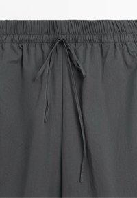 Dark gray elastic waistband pants with a tied drawstring visible at the center front and a smooth fabric texture.