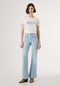 Vitt T-shirt med blå "Pepe Jeans London"-tryck, matchat med ljusblå utsvängda jeans med dekorativ sömnad på fickorna. Bruna klackskor.