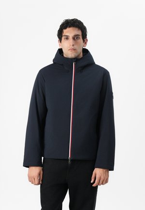 Chaqueta con capucha de color azul marino con cremallera frontal, presenta franjas de acento rojas y blancas, fabricada con un tejido ligero y con una textura suave.