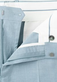 Lyseblå skræddersyede bukser med taljebånd, der viser lynlås, krog-og-stanglukning og en del af den hvide foring med knapdetalje.