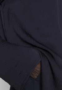 Tessuto testurizzato blu navy con un motivo sottile, caratterizzato da un orlo piegato e uno strato interno visibile in un colore a contrasto.