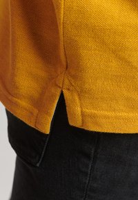 Gul bomulds T-shirt med struktureret stof, med sidesplitt og kontrastsyninger, parret med sorte denim.