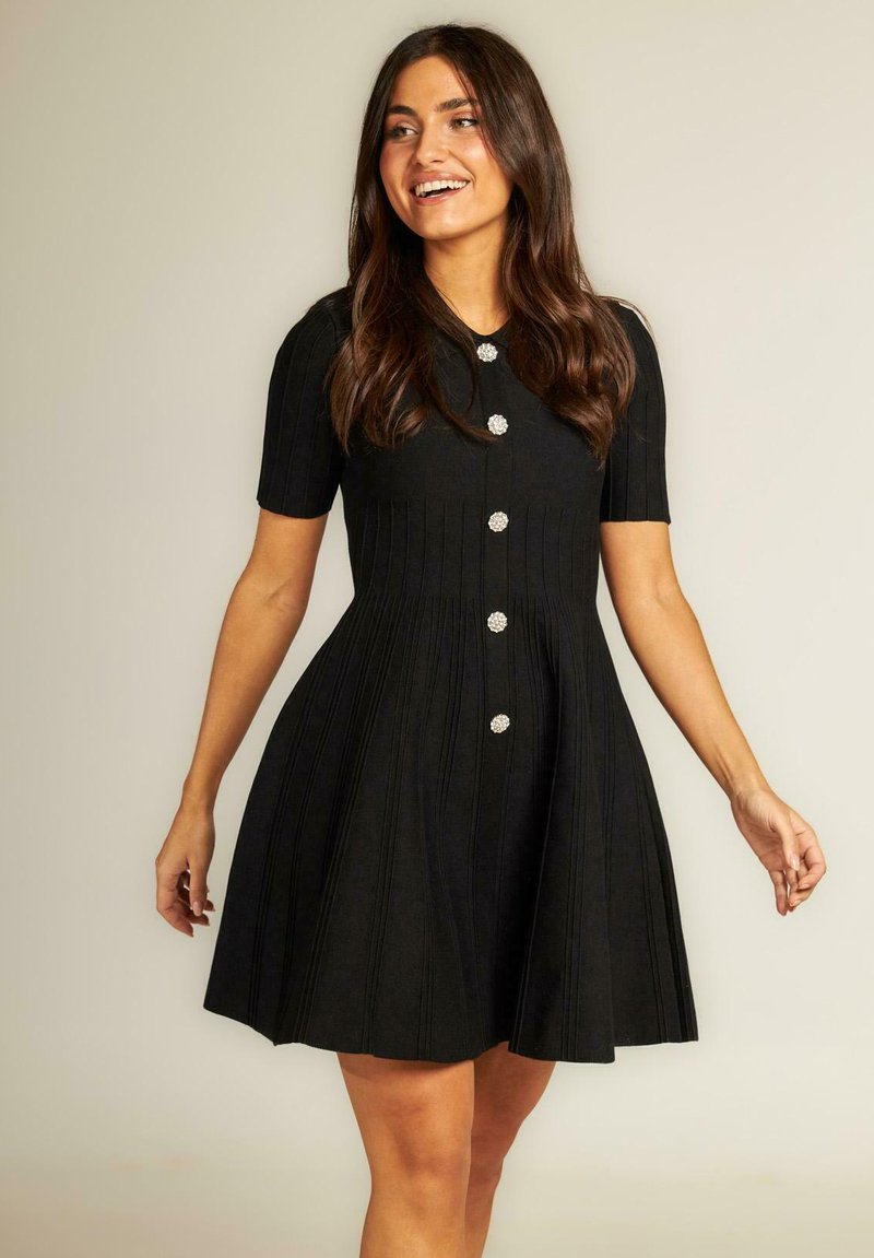 Vestido negro de manga corta con un cuerpo ajustado, falda acampanada, textura de canalé vertical y botones decorativos redondos a lo largo del frente.