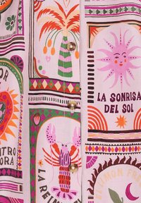 Tissu coloré présentant divers motifs, y compris des homards et des motifs de soleil, sur un fond rose clair avec des accents de boutons décoratifs.