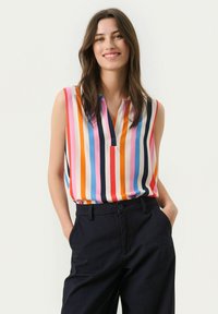 Sleeveless blouse in colorful vertical stripes, featuring a v-neckline and smooth fabric. Paired with navy trousers, showcasing a relaxed fit.