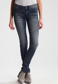 Mörkblå denim skinny jeans med en blekt tvätt, fem fickor och dragkedja, i kombination med svarta och vita leopardmönstrade ankelstövlar.