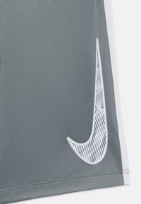 Sivé športové šortky s veľkým bielym logom Nike Swoosh a šikmými pruhmi na jednej strane. Tkanina má hladkú, ľahkú textúru.