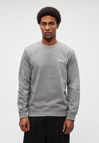 Sweatshirt cinzenta com decote redondo e mangas compridas. Apresenta uma pequena etiqueta da marca no peito. Material macio, design minimalista.