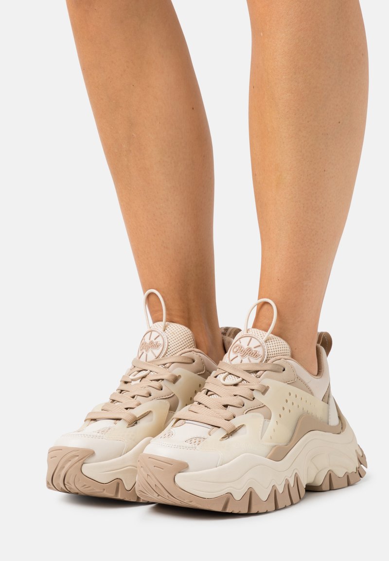 Beige og kremfargede sneakers med mesh- og lærdetaljer, teksturert såle, tykk, oppdriftende demping, og dekorativ branding på tungen.